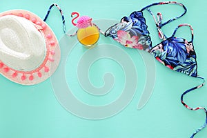Top view of fashion female swimsuit bikini and white fedora hat on mint wooden background. Summer beach vacation concept.