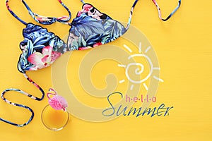Top view of fashion female swimsuit bikini on yellow wooden background. Summer beach vacation concept.