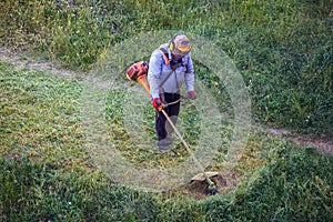 Top view fat dirty lawnmover man worker cutting dry grass with lawn mower photo