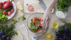 Top view of female chef cutting tomato and adding it into bowl with fresh salad