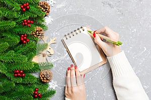 Top view of female hand writing in a notebook on cement Christmas background. fir tree and festive decorations. Wish list. New