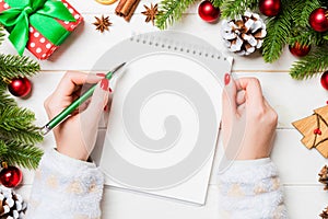 Top view of female hand writing in a notebook on wooden Christmas background. Fir tree and festive decorations. Wish list. New