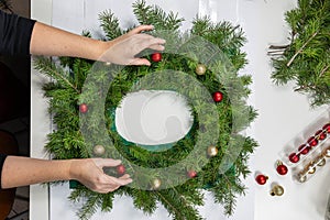 Top view female hands decorating a wreath with Christmas balls . DIY Christmas wreaths