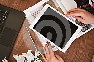 top view on female hands with digital tablet and stylist workplace, fashion magazines, smartphone, laptop