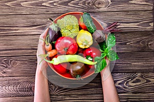 Top view female hands holding the bowl with different Fresh Farm Vegetables on the dark wooden background. Harvest. Food or Health