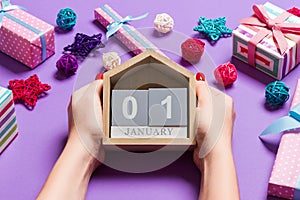 Top view of female hands holding calendar on purple background. The first of January. Holiday decorations. New Year concept