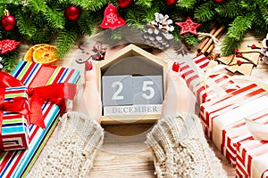 Top view of female hands holding a calendar on wooden background. The twenty fifth of December. Holiday decorations. Christmas