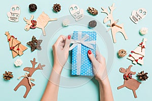 Top view of female hands holding a Christmas present on festive blue background. Holiday decorations and toys. New Year holiday