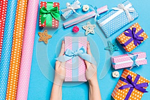 Top view of female hands holding a Christmas present on festive blue background. Holiday decorations and wrapping paper. New Year