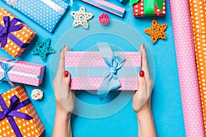 Top view of female hands holding a Christmas present on festive blue background. Holiday decorations and wrapping paper. New Year