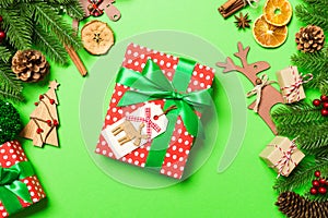 Top view of female hands holding a Christmas present on festive green background. Fir tree and holiday decorations. New Year