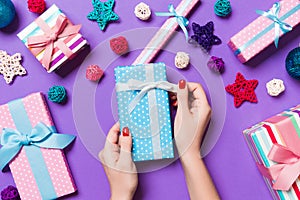 Top view of female hands holding a Christmas present on festive purple background. Holiday decorations, toys and balls. New Year