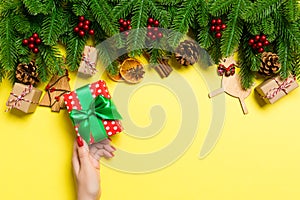 Top view of female hands holding a Christmas present on festive yellow background. Fir tree and holiday decorations. New Year