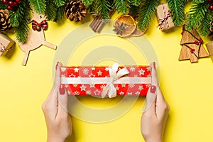 Top view of female hands holding a Christmas present on festive yellow background. Fir tree and holiday decorations. New Year