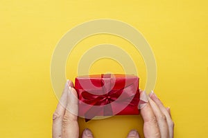 Top view of female hands holding gift red box with ribbon bow  over blue background, copy space