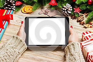 Top view of female hands holding a tablet on wooden Christmas background made of fir tree and festive decorations. New year