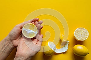 Top view of female hands holding whole and sliced ripe lemons on a yellow surface, concept of health and vitamins