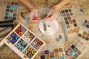 Top view of female hands making a macramÃ© bracelet with kumihimo on a wooden table with tools, spools of thread, natural stones