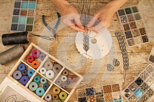 Top view of female hands making a macramÃ© bracelet with kumihimo on a wooden table with tools, spools of thread, natural stones