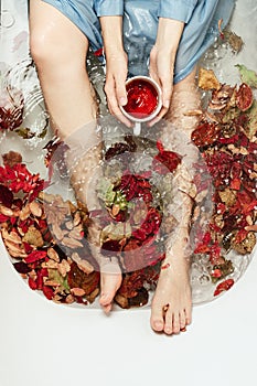 Top view of female holding cup of tea in a bath tub full of autumn leaves