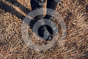 Top view of female legs, dressed in black, on dry grass.