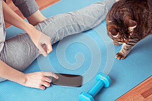 Top view of female person sitting on sports mat, touching empty screen of cellphone. Isolation period. Copy space at display of