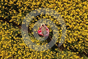 Top view of female rapeseed farmer examining blooming crops in field, aerial shot. Agronomist wearing red plaid shirt and trucker