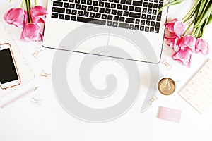 Top view of female worker desktop with laptop, flowers and different office supplies items. Feminine creative design workspace.