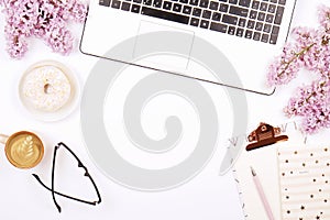 Top view of female worker desktop with laptop, flowers and different office supplies items. Feminine creative design workspace.