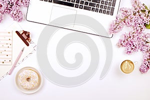 Top view of female worker desktop with laptop, flowers and different office supplies items. Feminine creative design workspace.