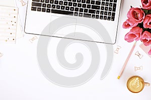 Top view of female worker desktop with laptop, flowers and different office supplies items. Feminine creative design workspace.