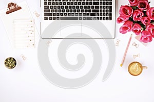 Top view of female worker desktop with laptop, flowers and different office supplies items. Feminine creative design workspace.