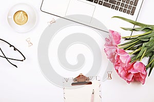 Top view of female worker desktop with laptop, flowers and different office supplies items. Feminine creative design workspace.