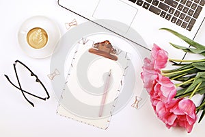 Top view of female worker desktop with laptop, flowers and different office supplies items. Feminine creative design workspace.