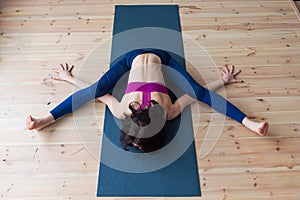 Top view of female yogi doing advanced kurmasana tortoise pose on mat indoors while practicing yoga