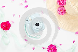 Top view feminine background with flowers and girl`s stuff. Flat lay modern instant camera, staw hat, ribbon, pink rose flowers o