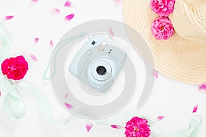 Top view feminine desk with flowers and girl`s stuff. Flat lay modern instant camera, staw hat, ribbon, pink rose flowers on whit
