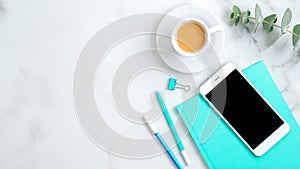 Top view feminine desktop with smartphone screen mockup, mint paper notebook, cup of coffee, office stationery and eucalyptus leaf