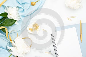 Top view feminine golden accessories, paper notepad, peony flowers on marble background. Minimal flat lay style wedding