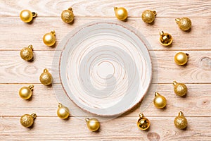 Top view of festive plate with golden baubles on wooden background. Christmas decorations and toys. New Year advent concept