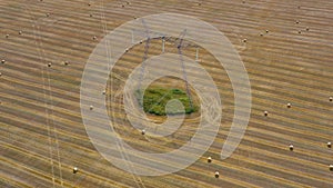 Top view of the field during haymaking. Round haystacks are scattered across the field. High voltage power lines cross