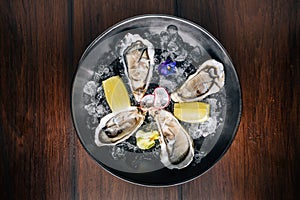 Top view of Fine de Claire Oyster and lemon served in black bowl with ice on wooden table photo