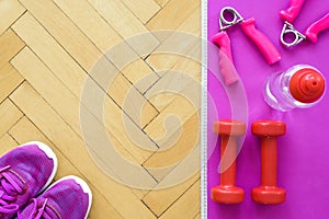 Top view of fitness equipment - pink mat for workout, two red dumbbells, bottle with water