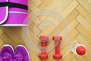 Top view of fitness equipment - pink mat for workout, two red dumbbells, bottle with water