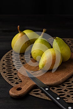 Top view of five green pears on wooden boards and knife, selective focus, black background,