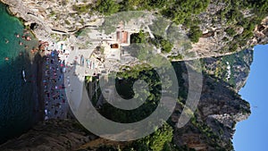 Top view from Fjord Furore Bridge to people relaxing and swimming on beach in Amalfi Coast on summer sunny day. Scenic