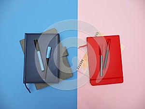 Top view flat lay of blue and red notebooks and pens on blue-pink background