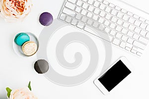 Top view flat lay colorful macarons with keyboard, cell phone and pink peonies on white table. Creative dessert concept