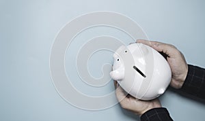 Top view flat lay design , Businessman holding white piggy saving bank on blue background for money saving and financial