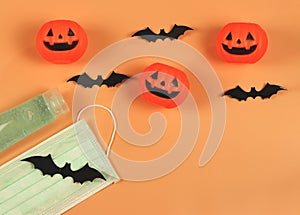Flat lay of Halloween pumpkin , black paper bats,medical mask and alcohol sanitizer gel on orange background. Halloween , COVID-19